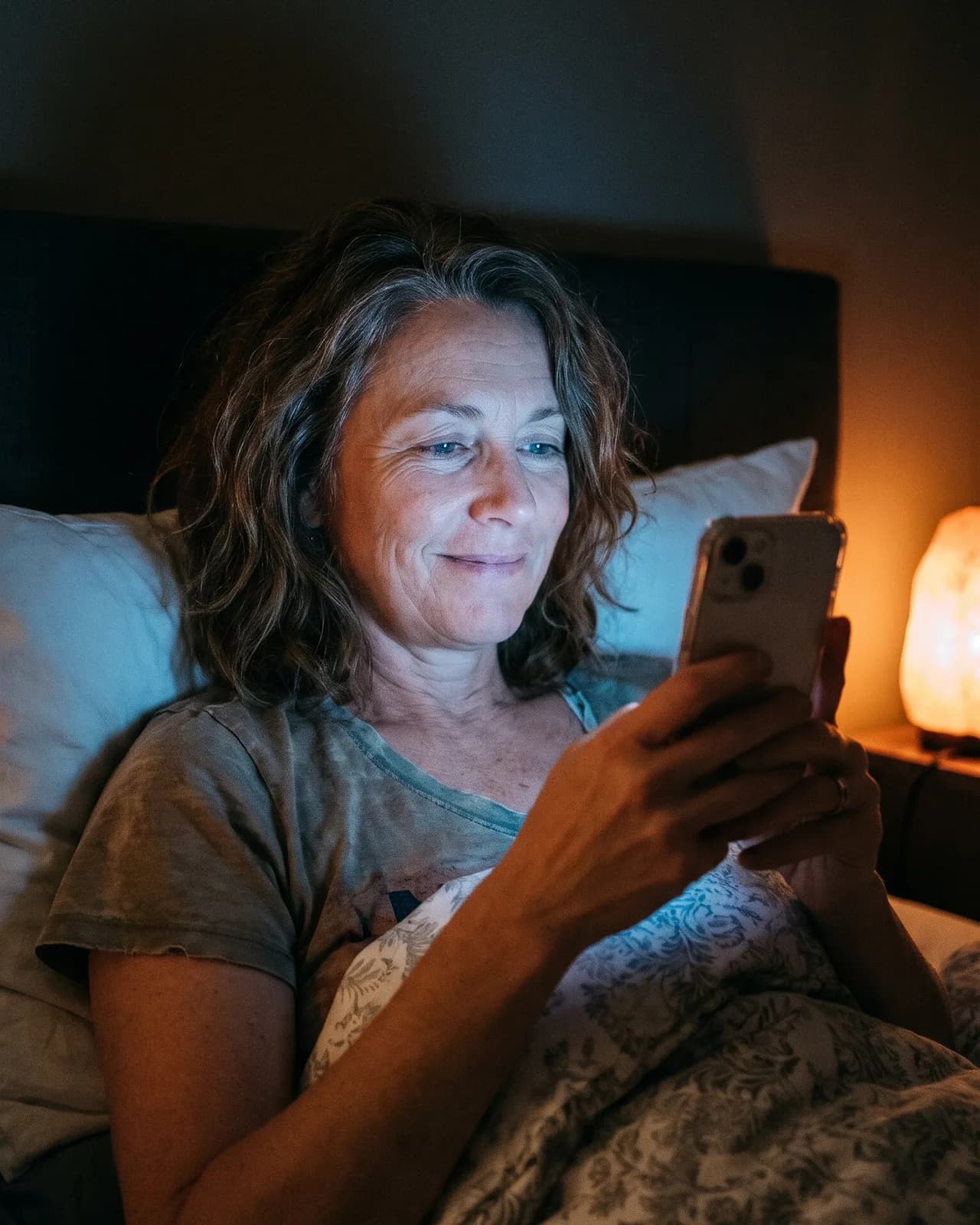 A woman in her fifties in bed at night, calm, reading her sleep protocol on her phone A woman in her fifties in bed at night, calm, reading her sleep protocol on her phone
